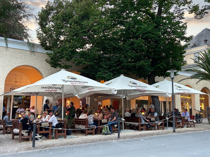 Biergarten des Pyrmonter Stadl unter den Arkaden an der Hauptallee, Sonnenschirme und besetzte Tische am Abend